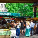 Busy outdoor market scene at Borough Market with colorful stalls and shoppers browsing under green canopies.