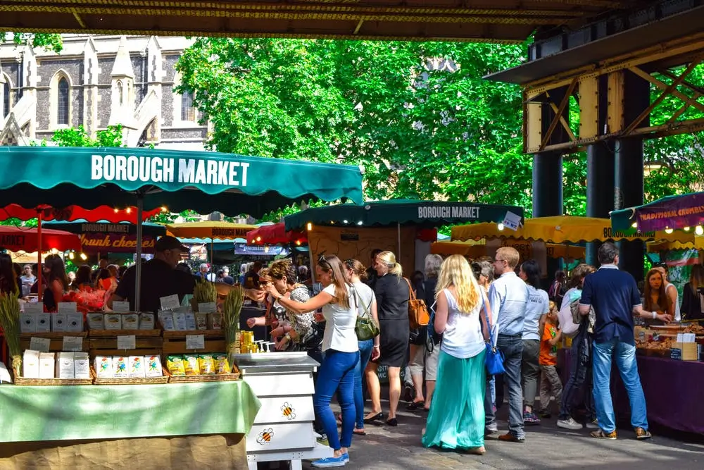 Busy outdoor market scene at Borough Market with colorful stalls and shoppers browsing under green canopies.